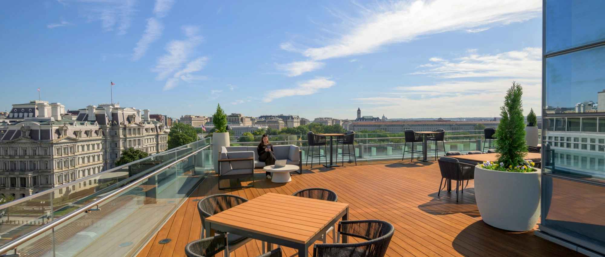 Rooftop terrace with modern outdoor seating, glass railings, and panoramic city views under a bright blue sky