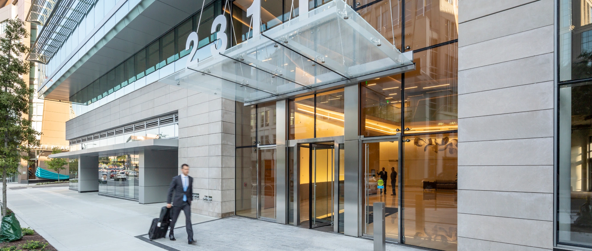 Sleek commercial building facade showing transparent lobby entrance, sidewalk activity, and modern architectural details