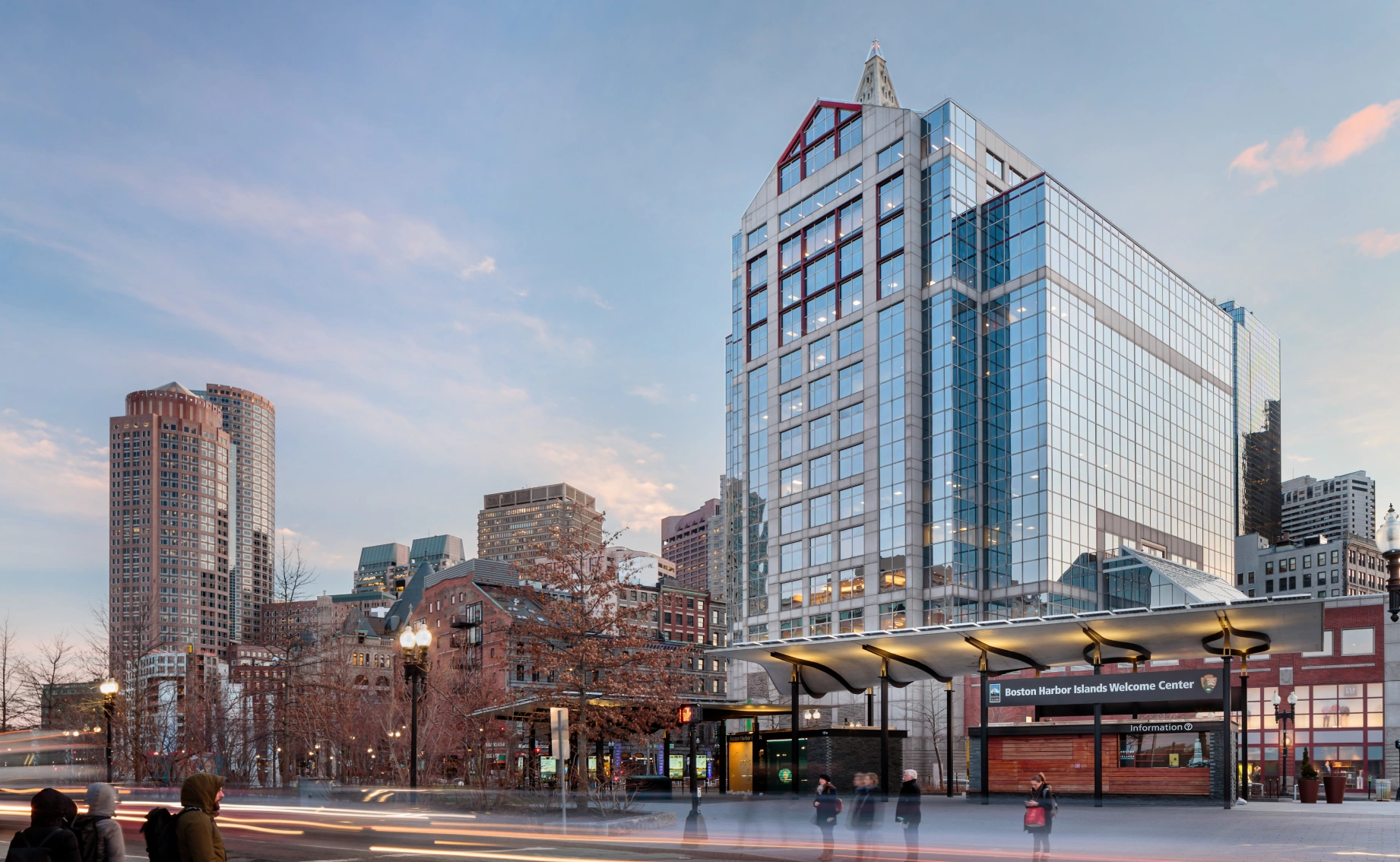 Contemporary waterfront skyscraper with reflective facade, evening sky, urban streetscape, and nearby public transit