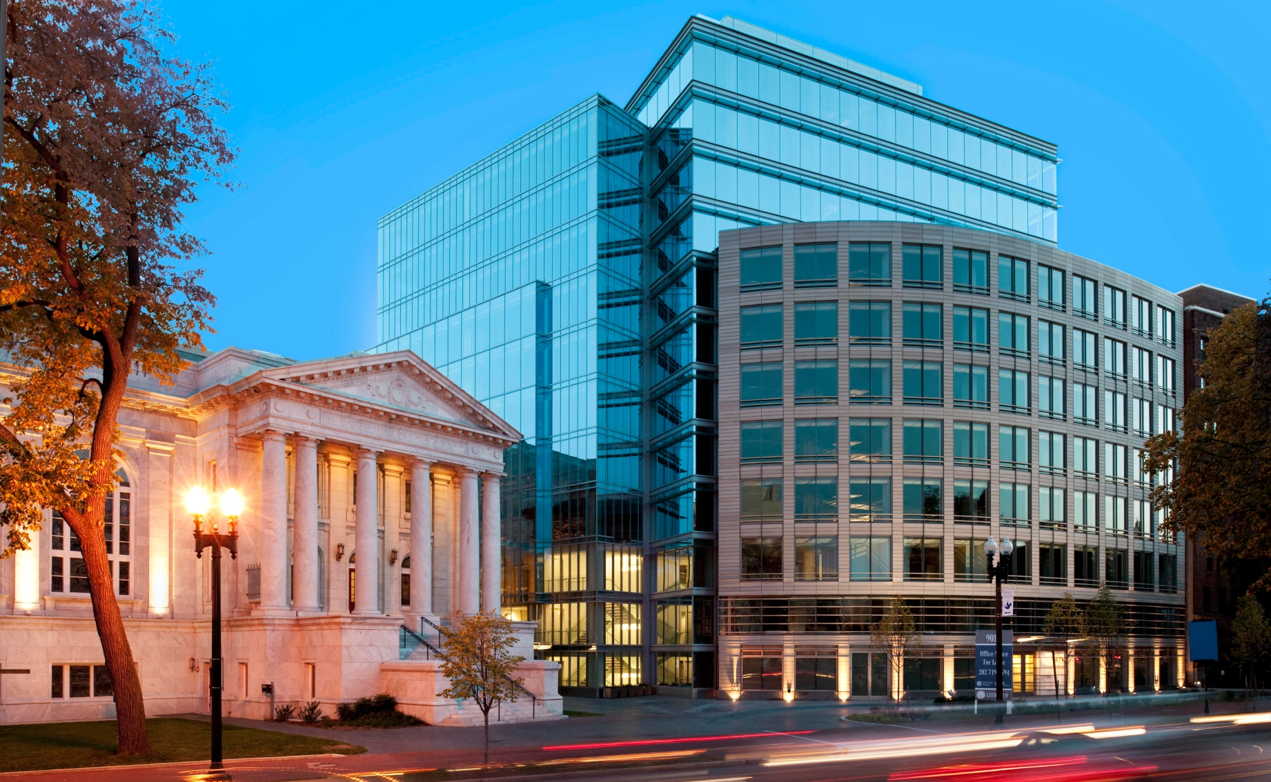 Striking urban architecture blending a modern glass office building with a historic neoclassical structure at dusk