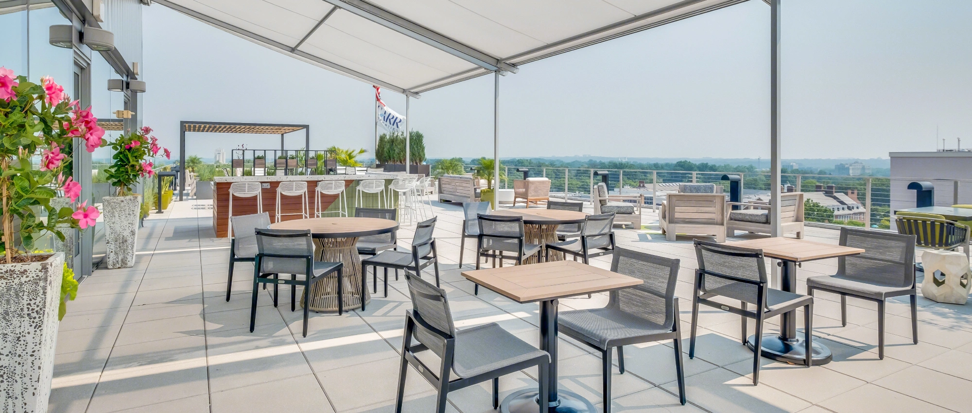 Stylish rooftop patio with covered seating, modern furniture, landscaped plants, and panoramic city backdrop