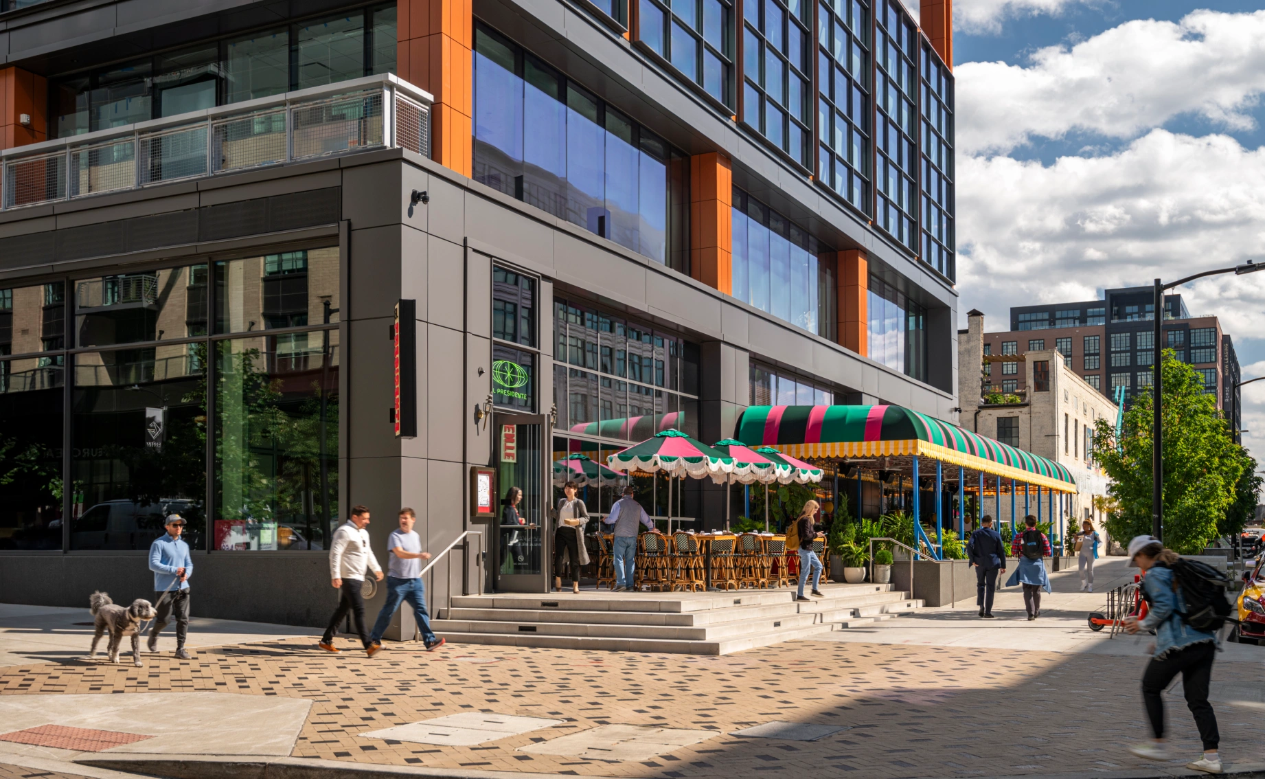 Contemporary mixed-use building featuring expansive glass façades, outdoor dining, and pedestrian-friendly streetscape