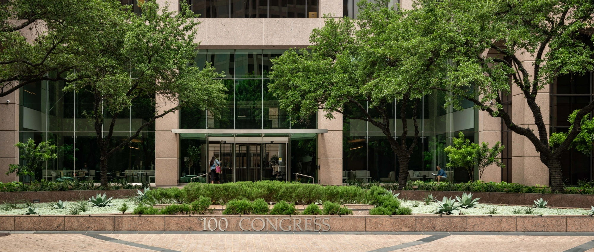 Corporate office exterior featuring 100 Congress signage symmetrical landscaping and reflective glass walls