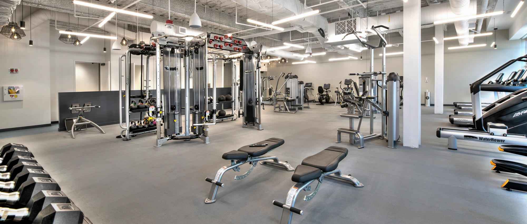 Contemporary office gym showcasing functional training equipment, weight benches, treadmills, and bright linear lighting