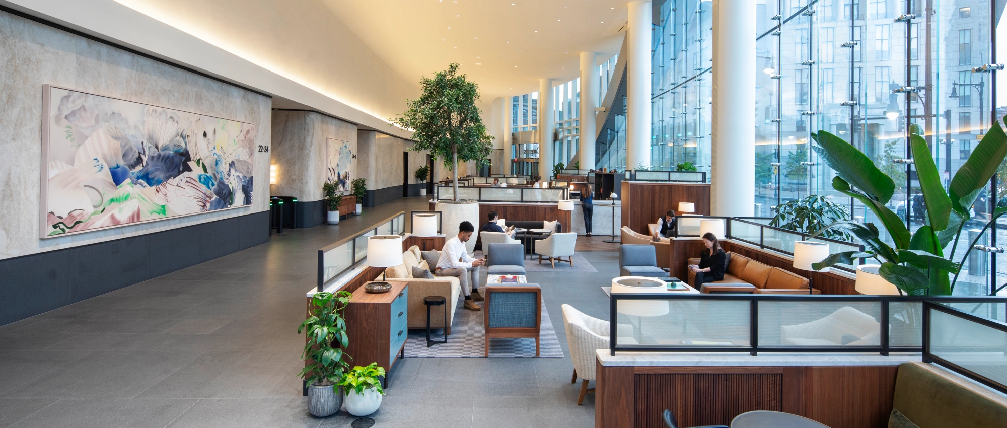 Spacious corporate atrium featuring lounge seating artwork greenery and floor to ceiling windows
