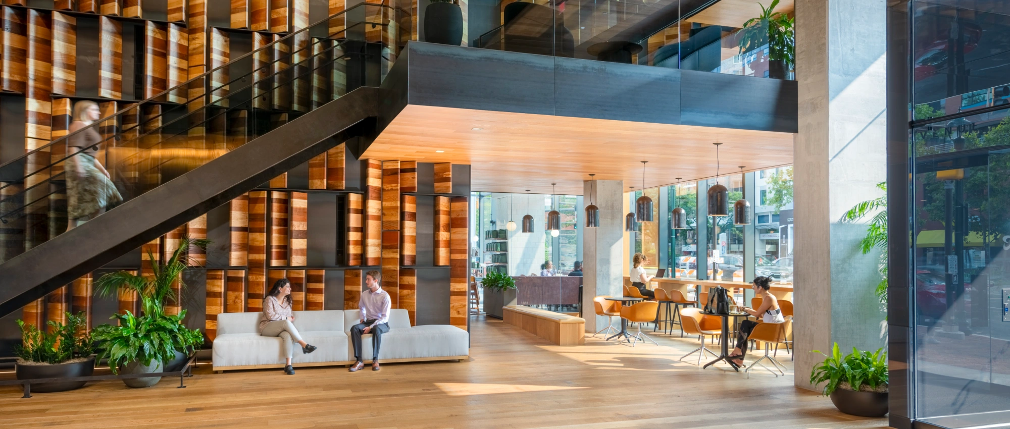Contemporary mixed use building lobby featuring staircase warm wood finishes greenery and collaborative seating
