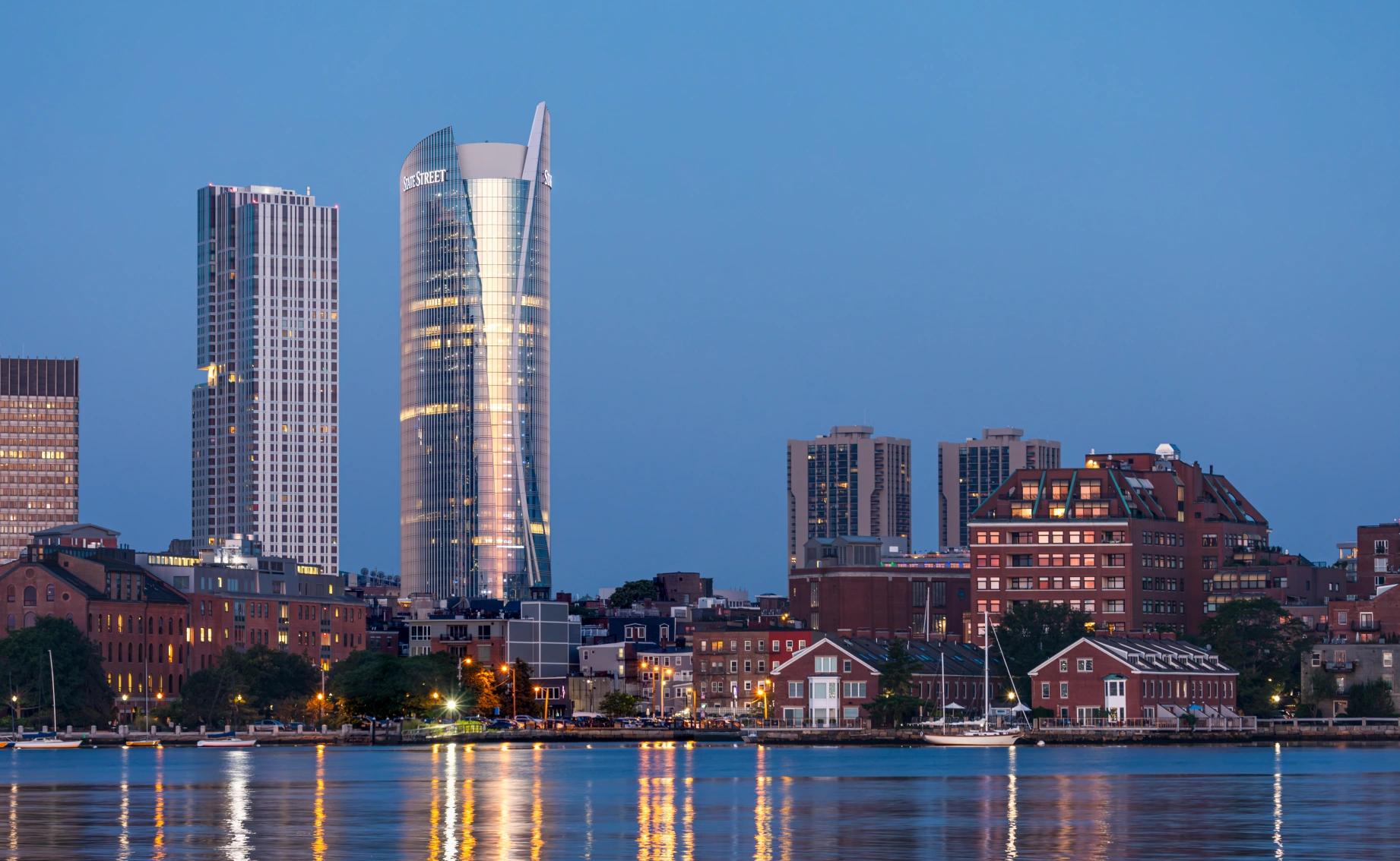 Evening view of Boston skyline with State Street skyscraper illuminated above historic waterfront buildings