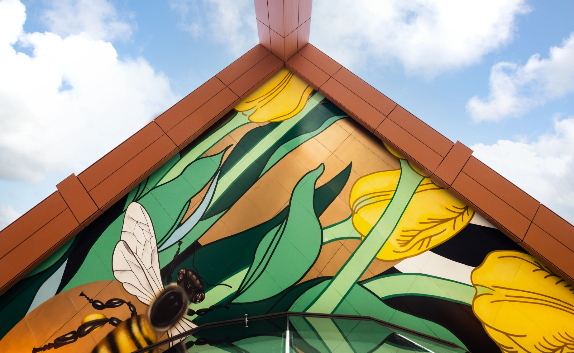 Close-up architectural detail of a modern building corner featuring a vibrant mural of yellow flowers and a bee framed by bold orange metal