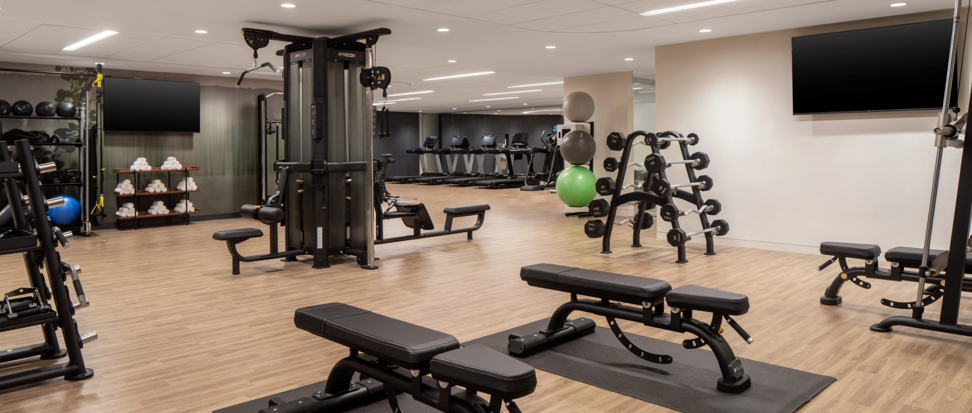 Spacious, well-lit gym with weight benches, cable machines, and treadmills in a contemporary design