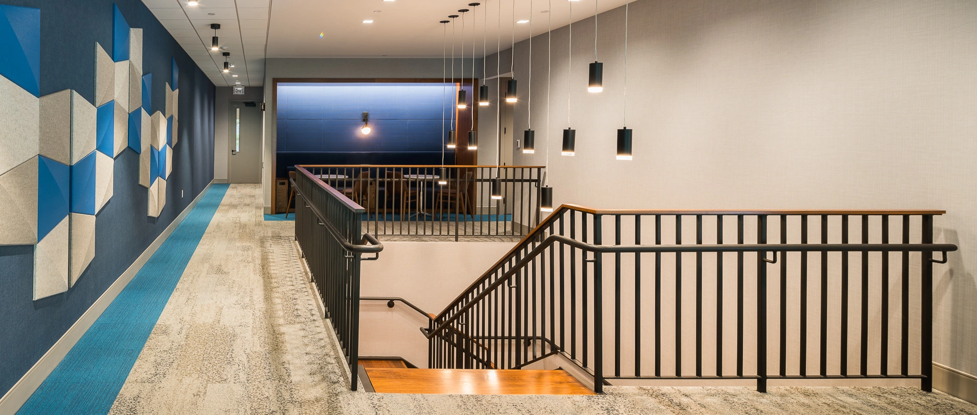 Stylish interior corridor with staircase, black metal railings, textured carpet, and minimalist architectural lighting