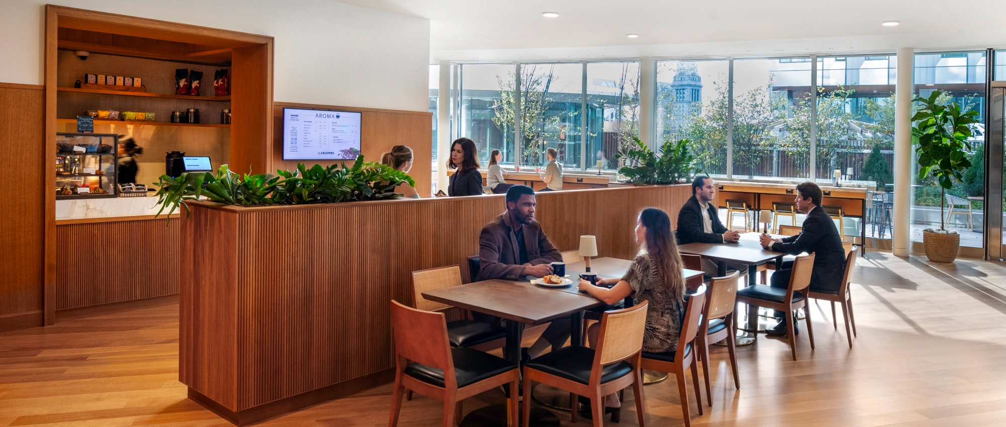 Contemporary workplace coffee bar featuring communal tables warm lighting greenery and casual business conversations