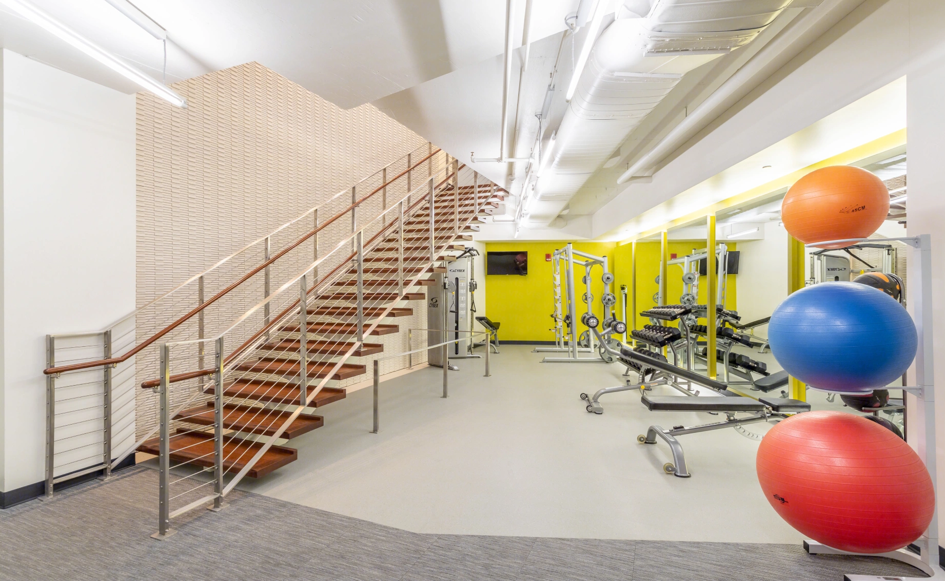 Contemporary gym space featuring open stair design, strength machines, free weights, and clean minimalist finishes