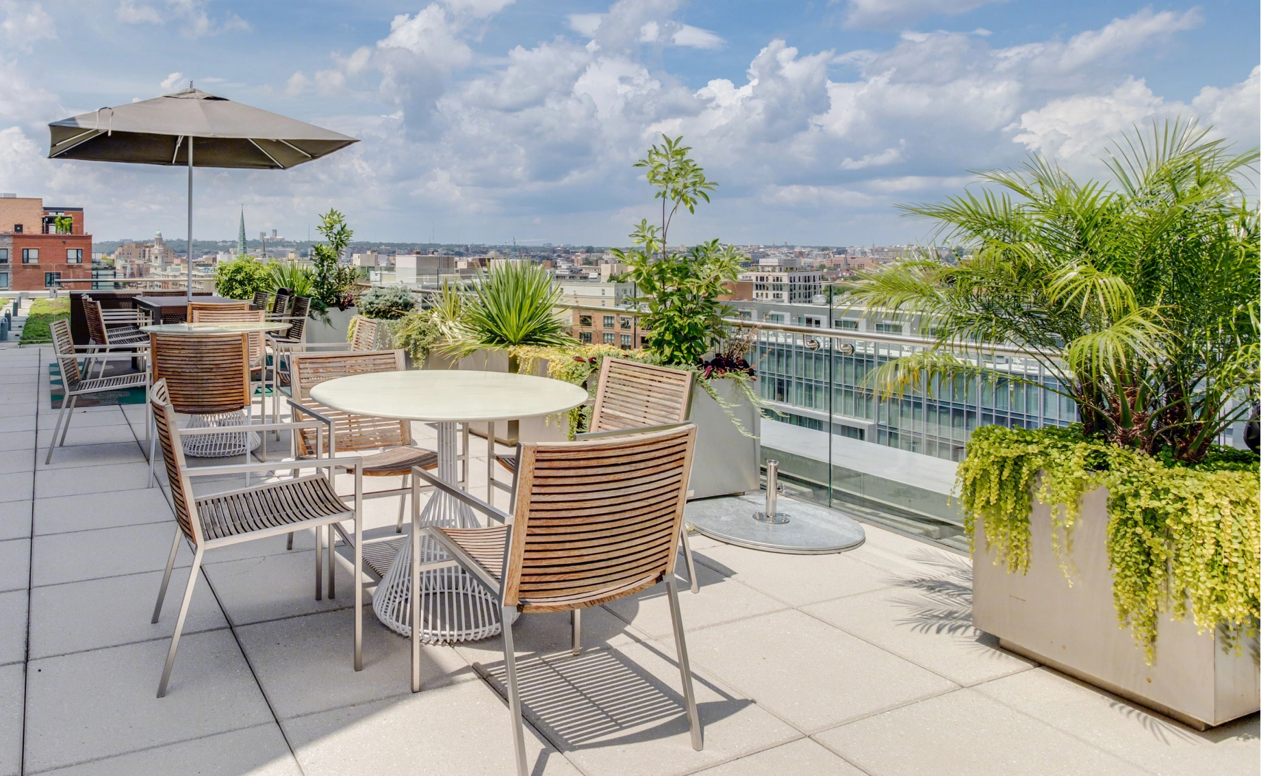 Rooftop terrace with modern outdoor seating, lush planters, and expansive city skyline views under a bright sky