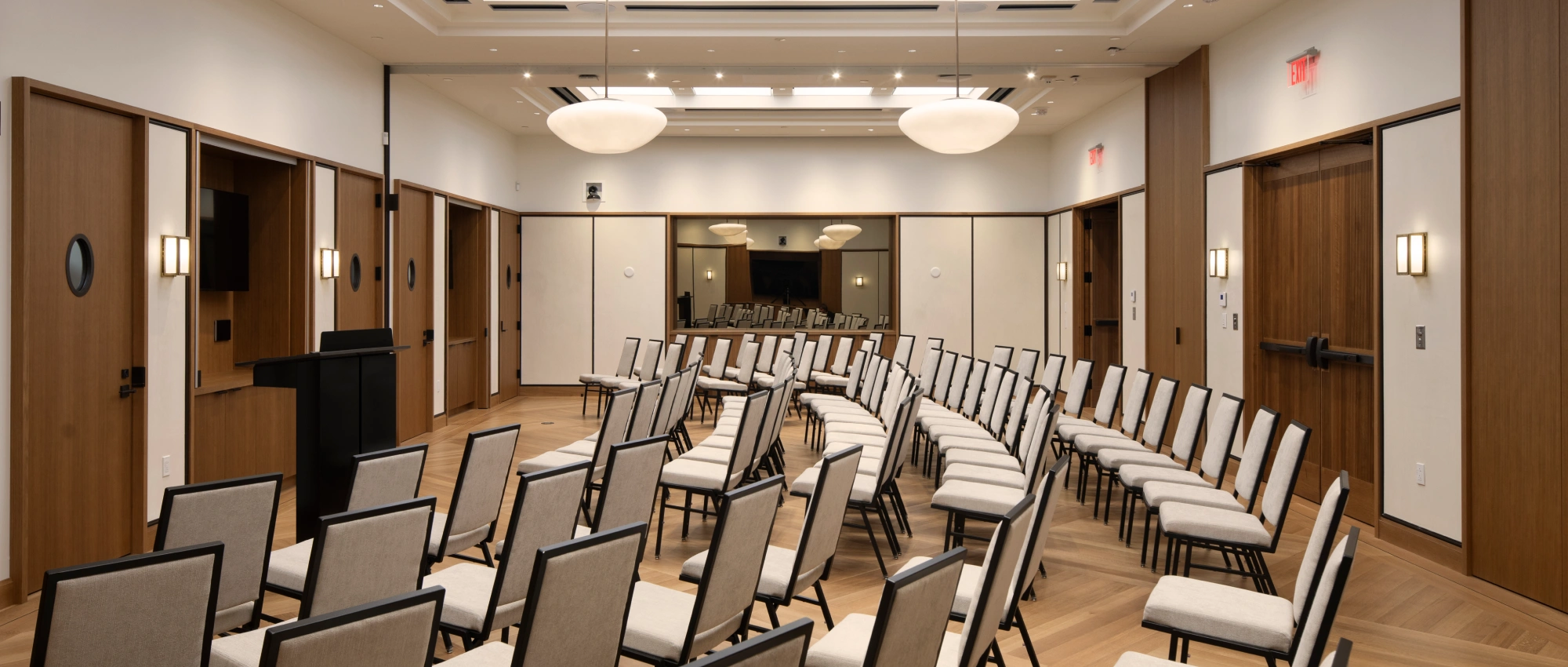 Flexible meeting space featuring rows of upholstered chairs presentation podium and warm contemporary finishes
