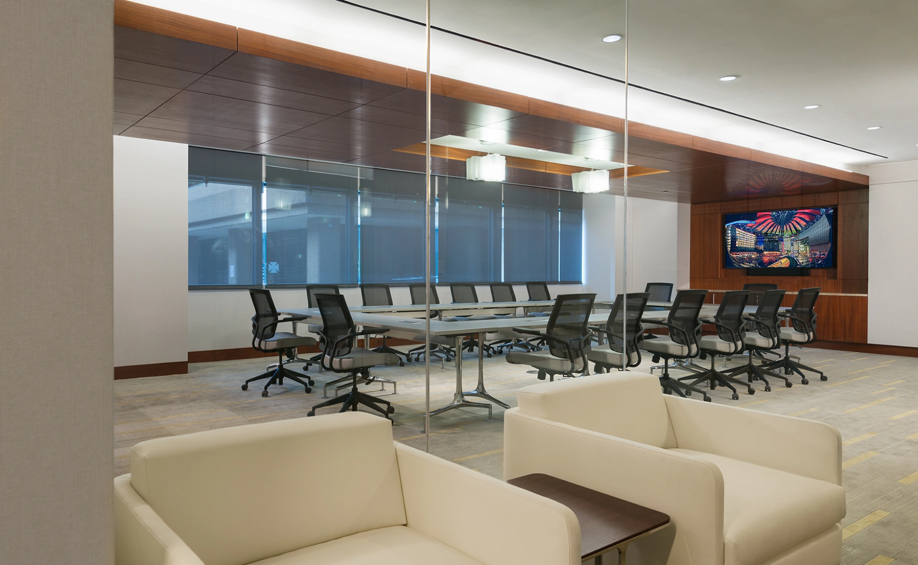 Modern corporate conference room viewed through glass walls with long table ergonomic chairs and display screen