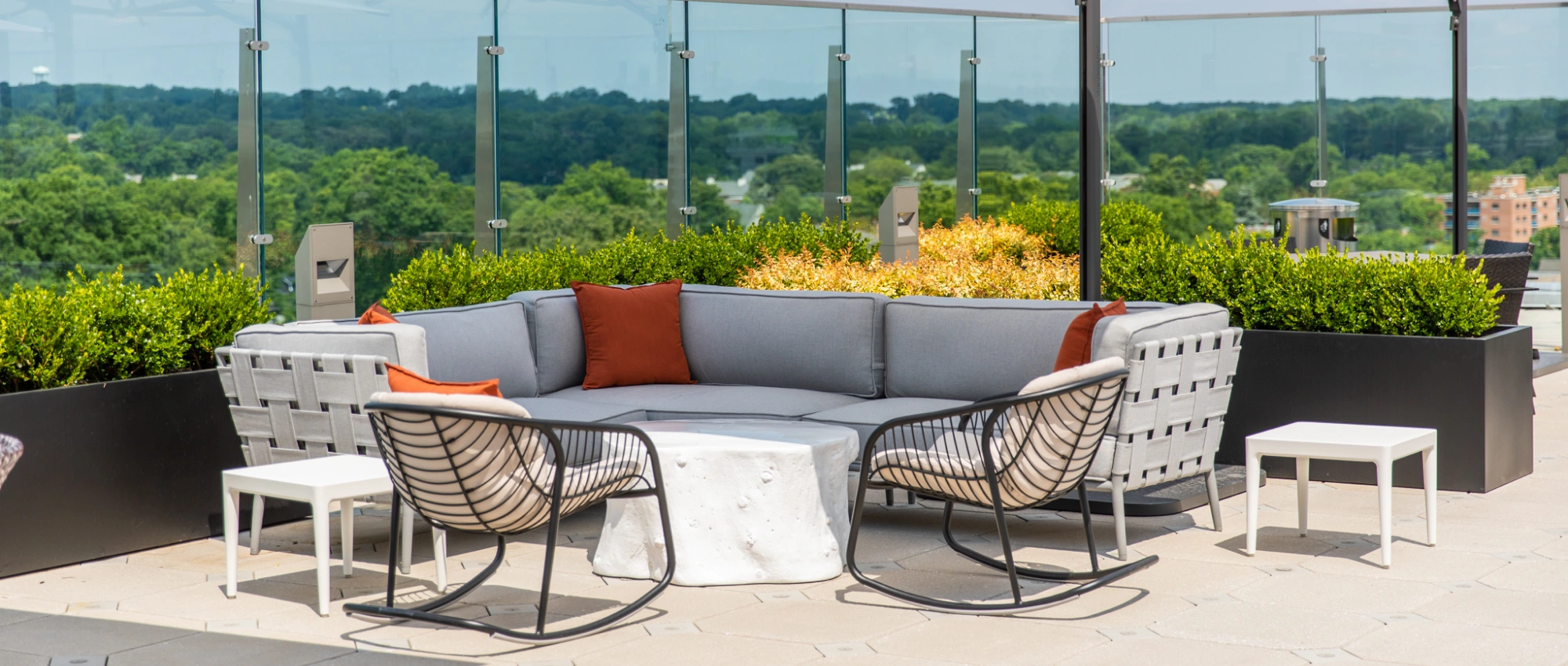 Contemporary rooftop lounge with cushioned seating, accent pillows, planter greenery, and panoramic suburban backdrop