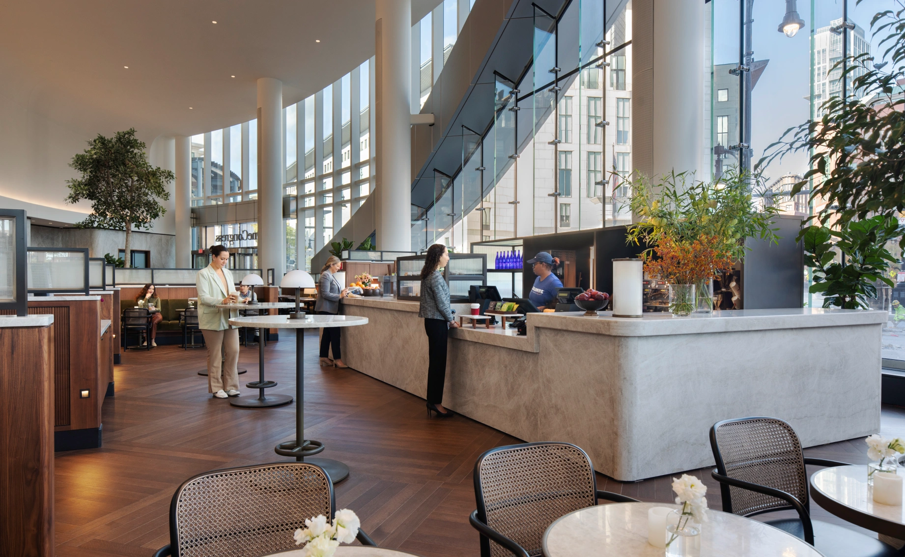 Contemporary office atrium café featuring warm wood flooring, biophilic accents, and casual meeting spaces