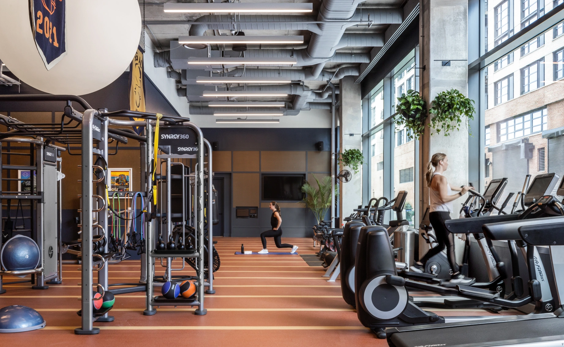 Contemporary gym space featuring functional training rigs, treadmills by floor-to-ceiling windows, and an industrial design aesthetic
