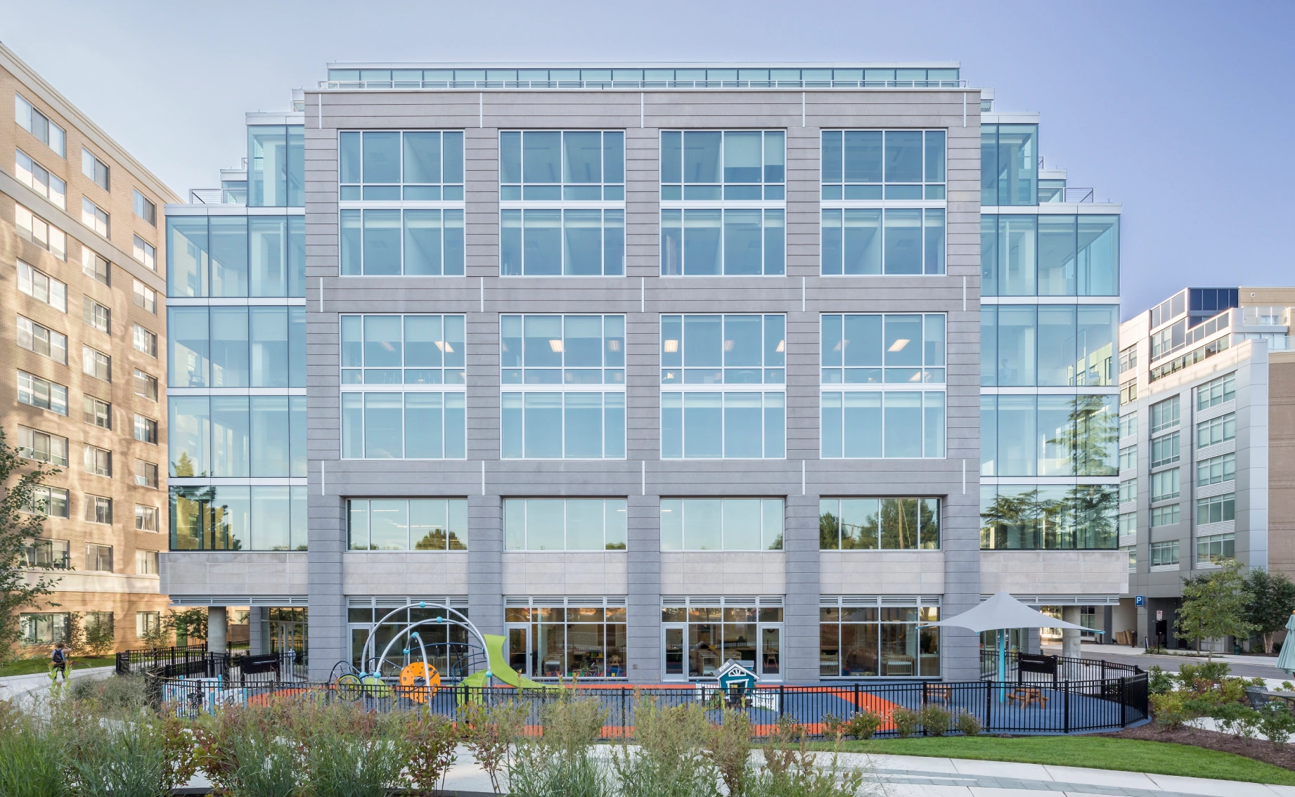 Modern mid-rise office building with expansive glass facade, landscaped courtyard, and outdoor amenity space