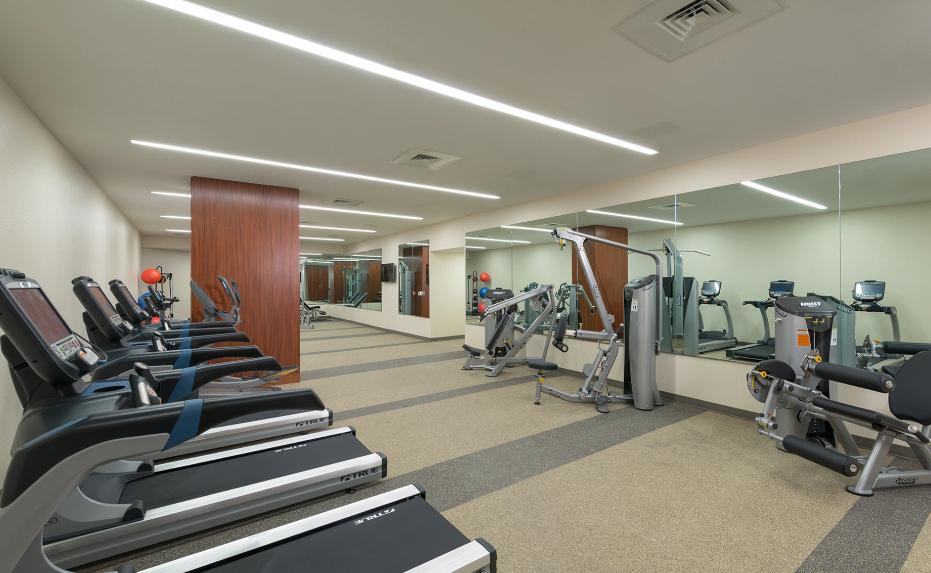 Corporate gym facility featuring cardio equipment weight machines full wall mirrors and bright linear lighting