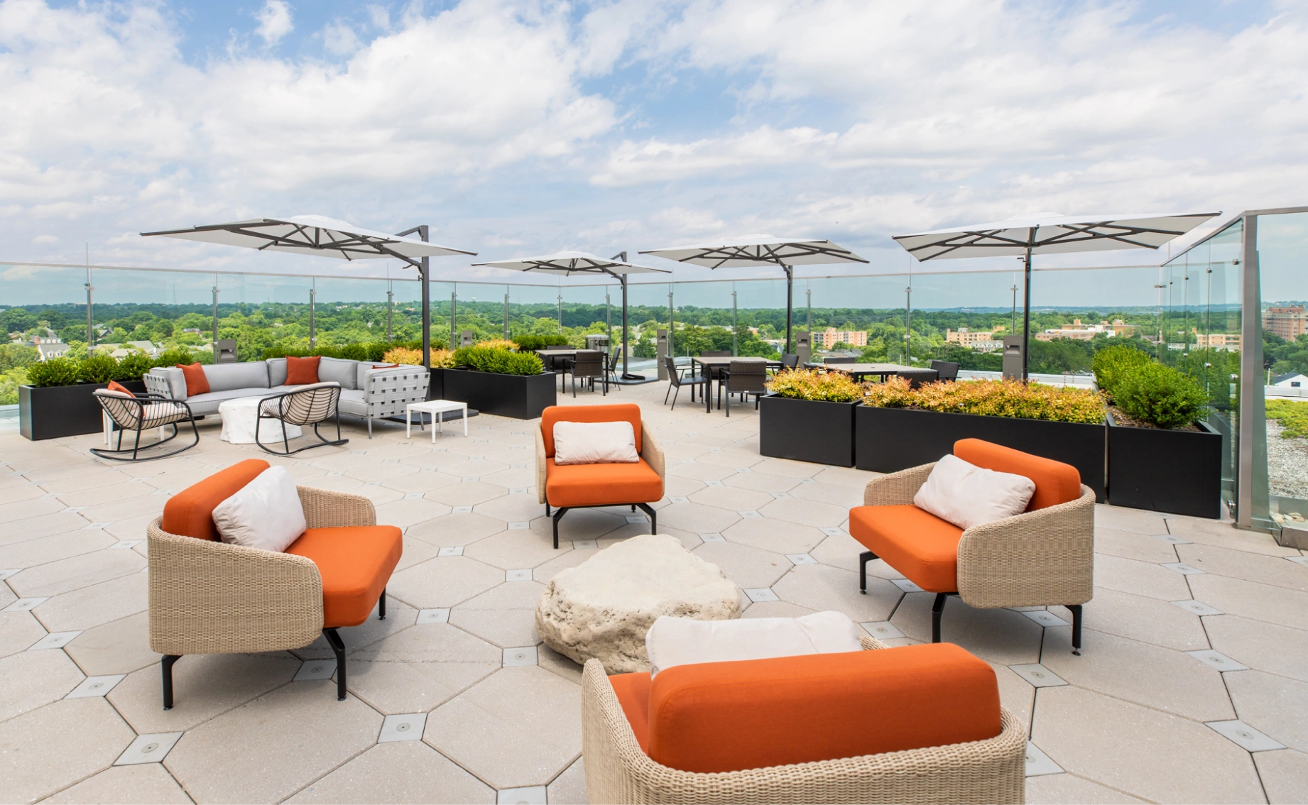 Contemporary rooftop amenity space featuring cushioned lounge chairs, umbrellas, and landscaped planters
