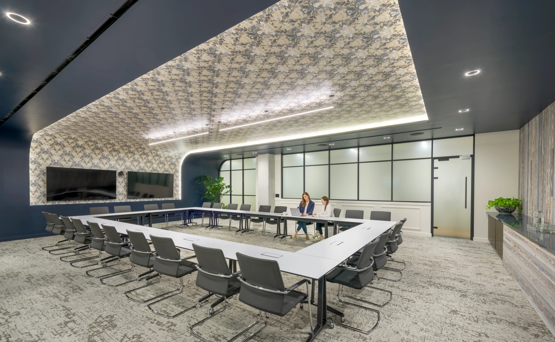 Contemporary boardroom interior featuring sleek seating, large displays, textured ceiling design, and minimalist décor