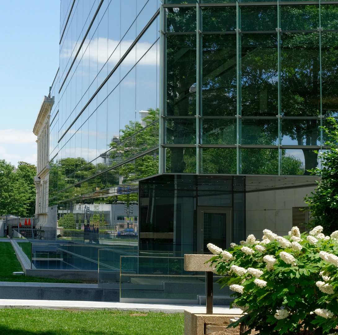 Contemporary architectural façade featuring floor to ceiling glass, urban greenery, and minimalist exterior detailing