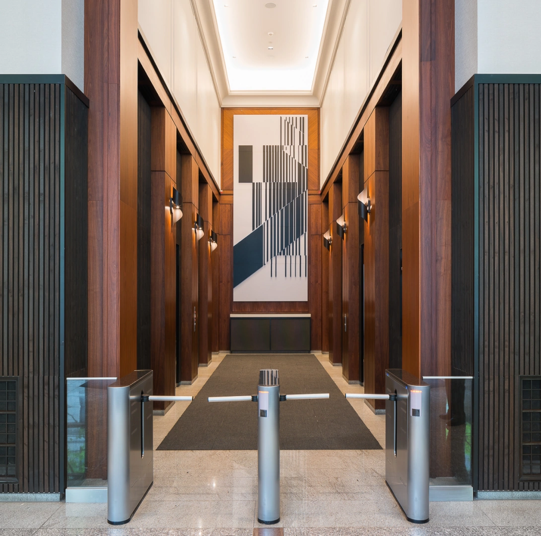 Modern corporate lobby corridor featuring elevator banks, access control gates, warm lighting, and refined finishes