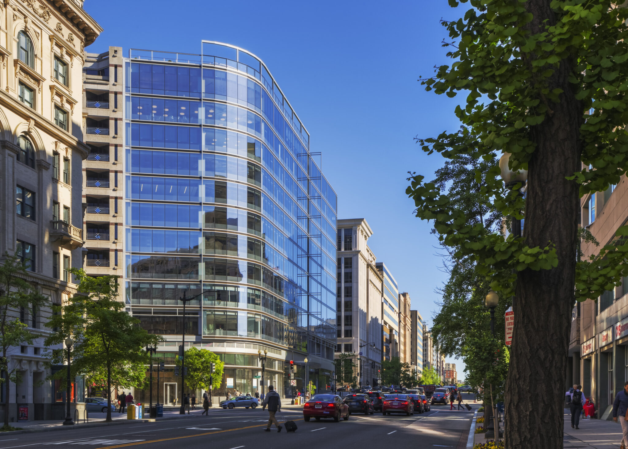 Modern glass office building with curved facade along downtown street with traffic and pedestrians