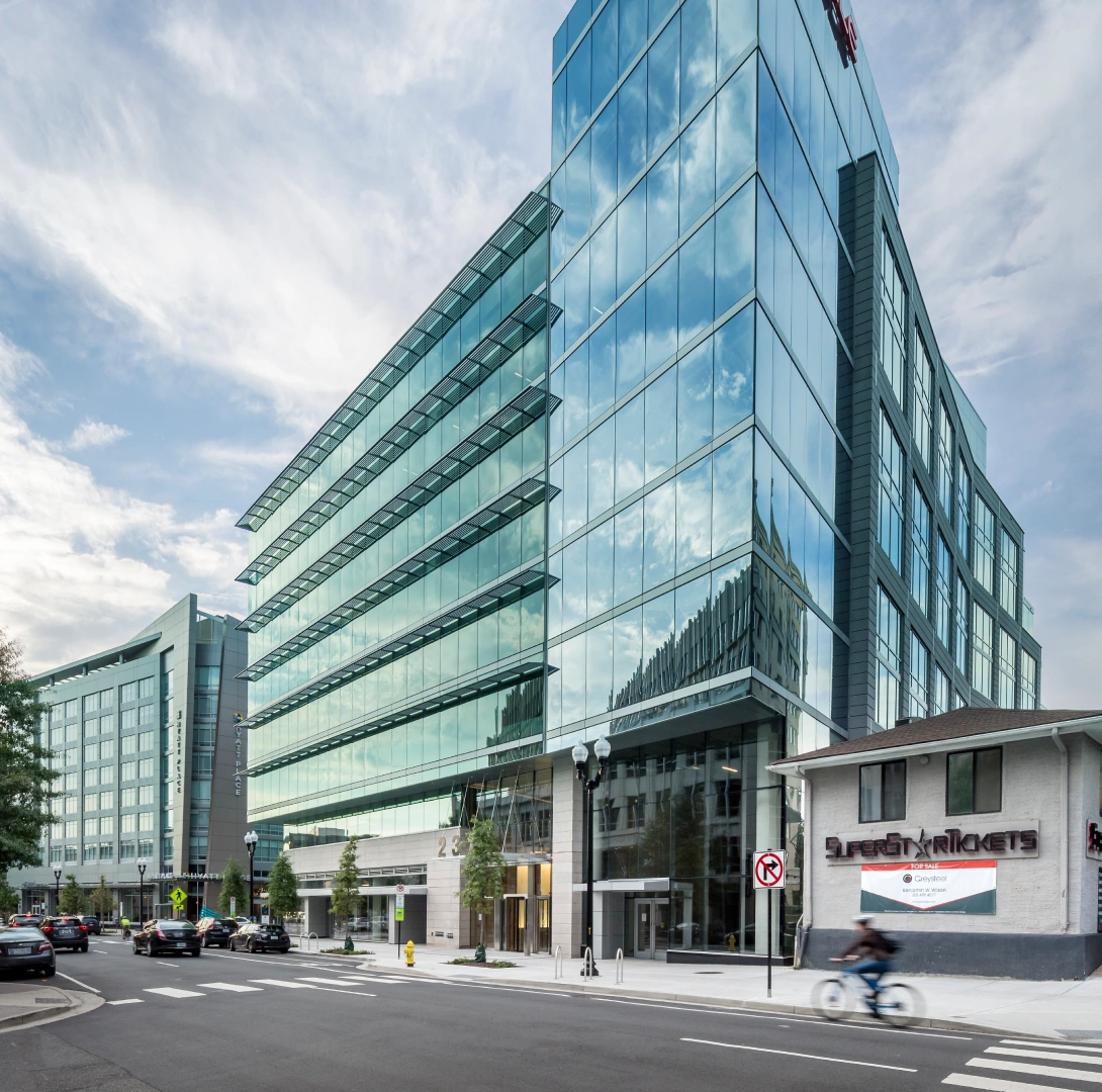 Modern glass office tower with reflective facade, street level entrance, and active urban streetscape