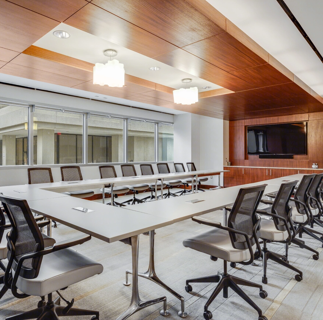 Modern executive boardroom with U-shaped conference table, ergonomic chairs, wood ceiling panels, and built-in display