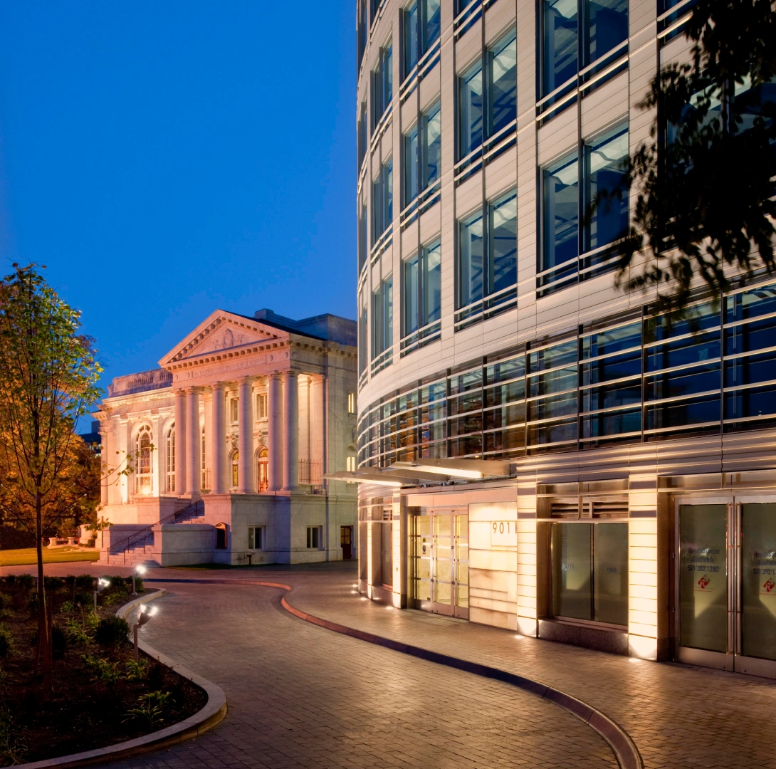 Urban office complex at twilight featuring sleek glass architecture dramatic lighting and a landscaped pedestrian approach