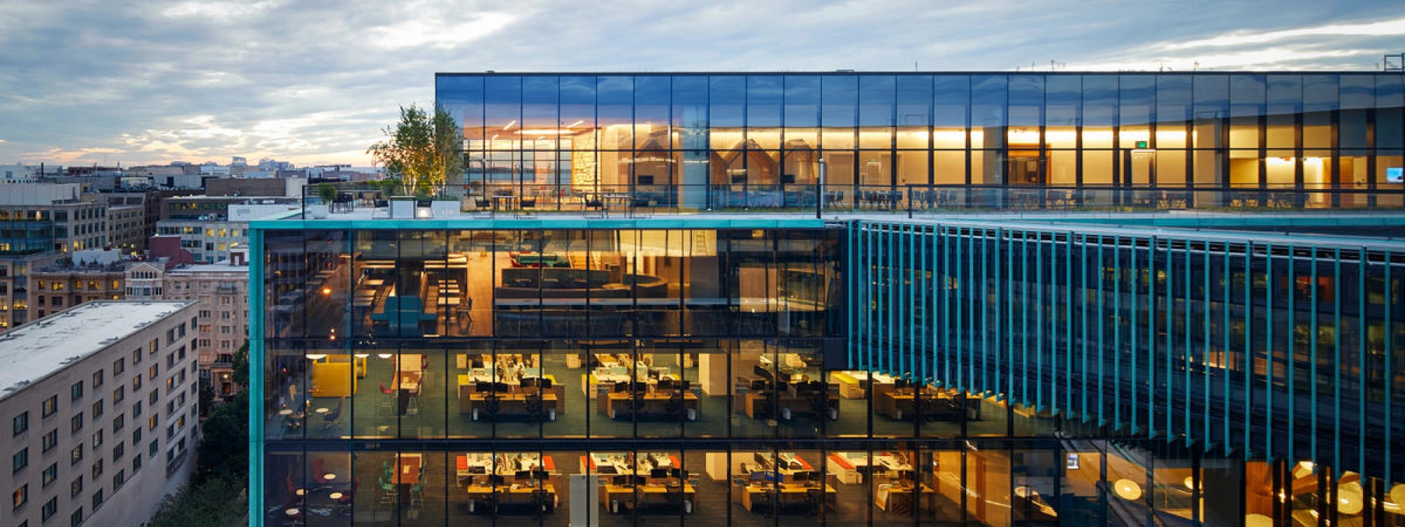 Contemporary corporate headquarters with transparent facade revealing active office interiors at evening