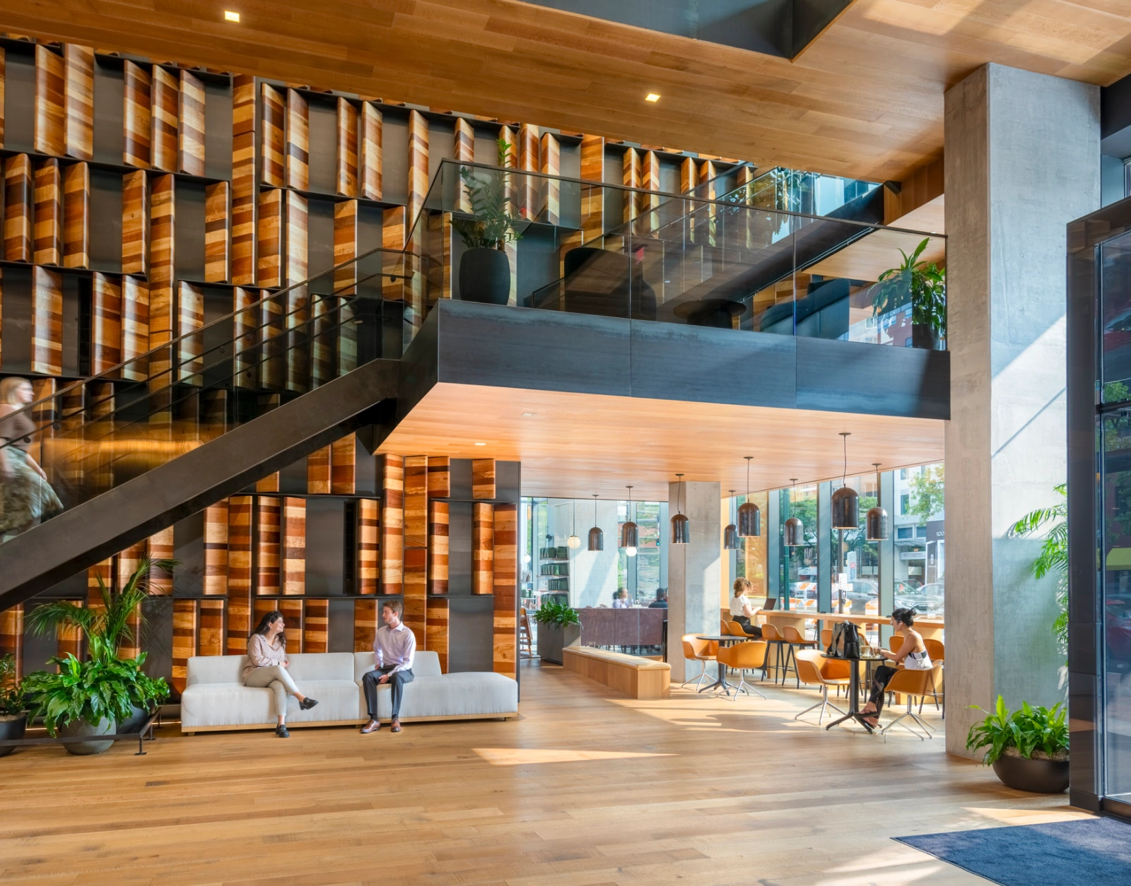Contemporary workplace atrium featuring warm wood finishes collaborative seating glass railings and natural light