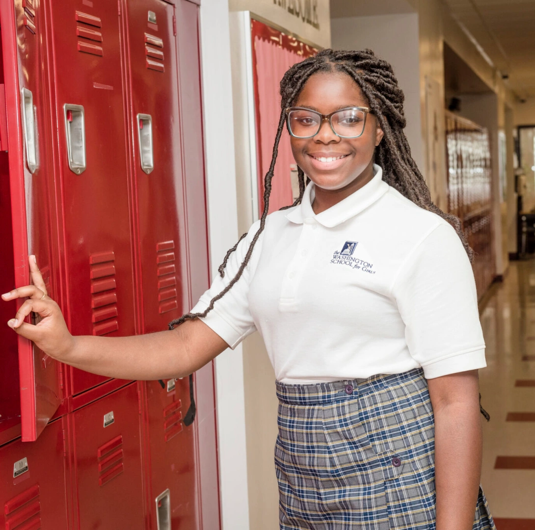 Middle school student standing at lockers in private school hallway wearing plaid uniform