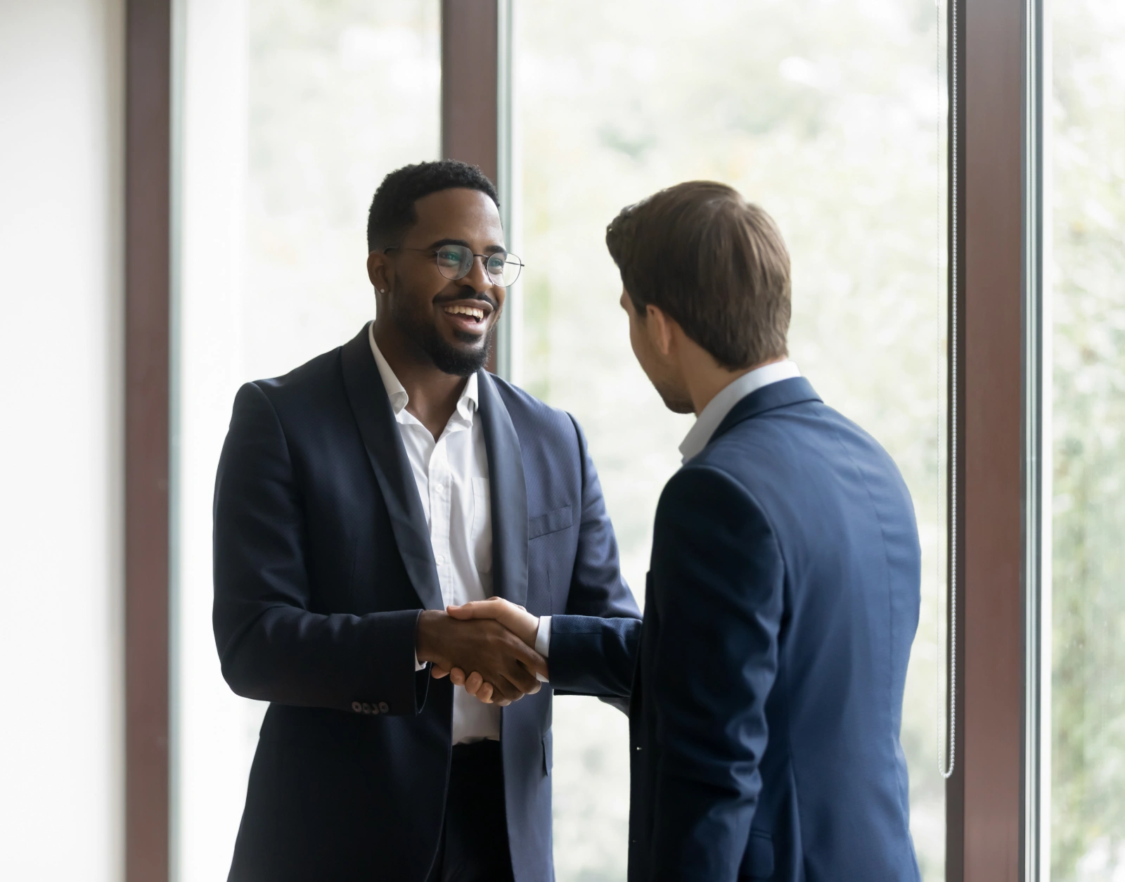 Business partners shaking hands near office windows celebrating collaboration and positive professional relationship