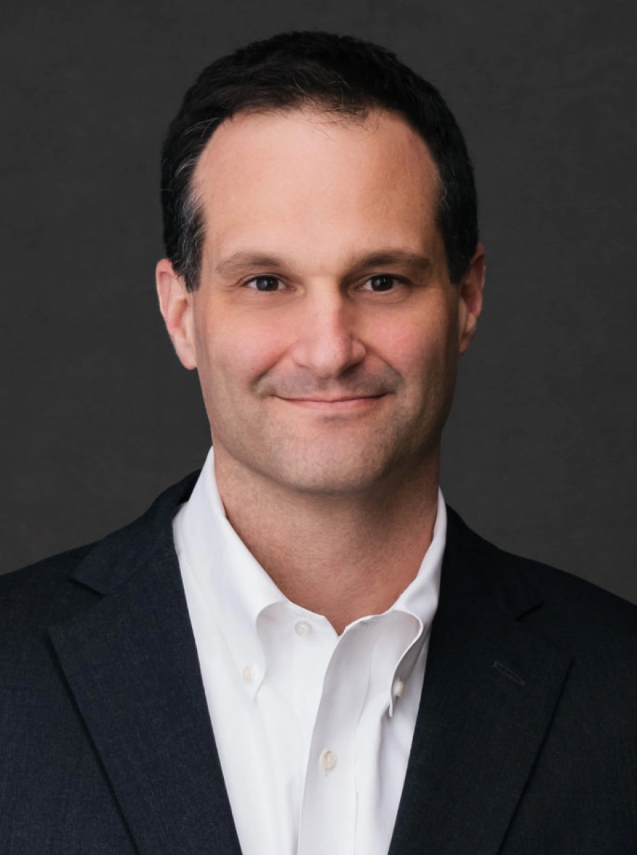 Professional corporate headshot of confident male executive wearing white shirt and dark blazer