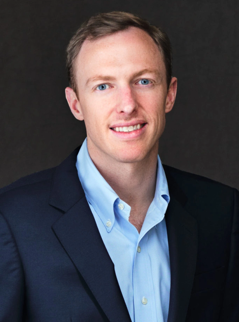 Professional business headshot of confident male executive wearing blazer against neutral studio background