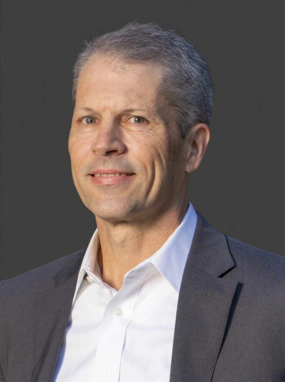 Corporate leadership portrait featuring confident professional man with silver hair against neutral background