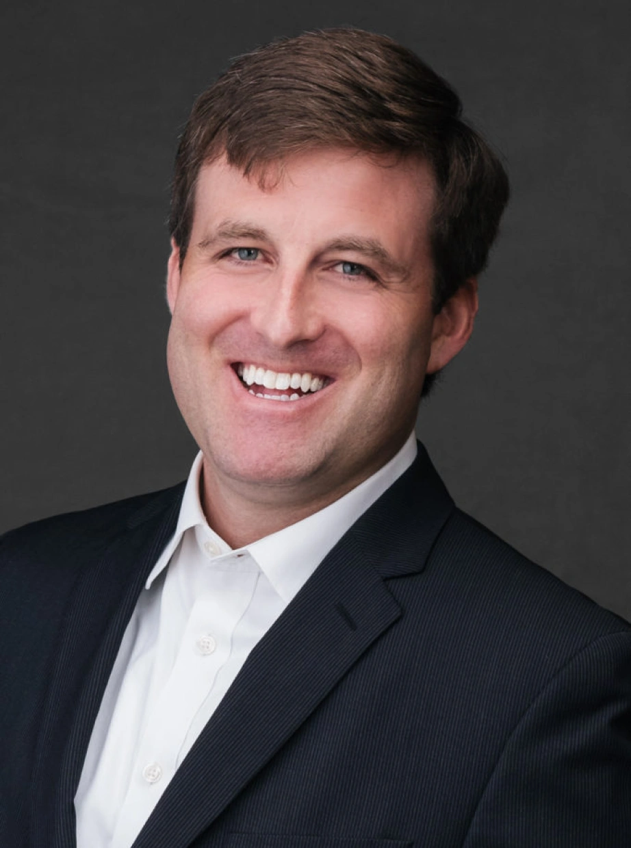 Corporate executive portrait featuring approachable professional man smiling against neutral studio background