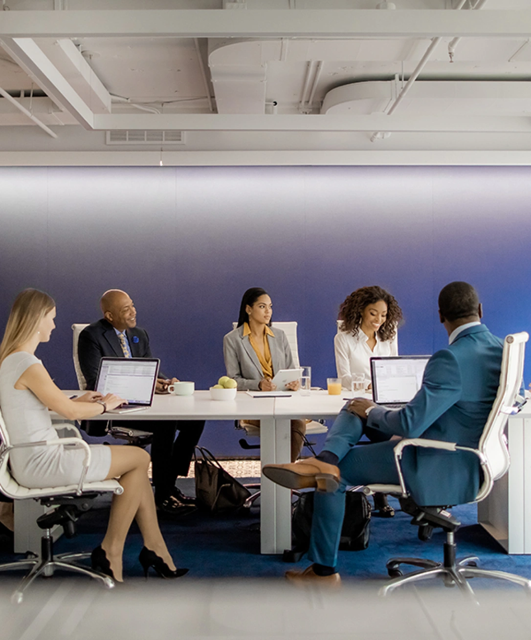 Corporate team meeting with executives seated around conference table using laptops and tablets