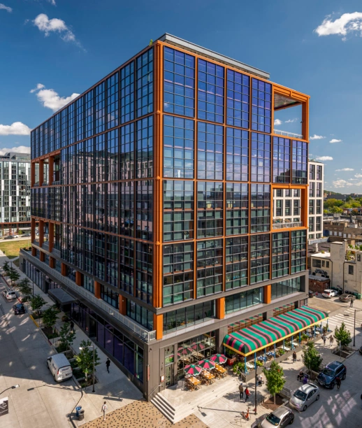 Modern glass office building with bold orange framing above street level retail and sidewalks