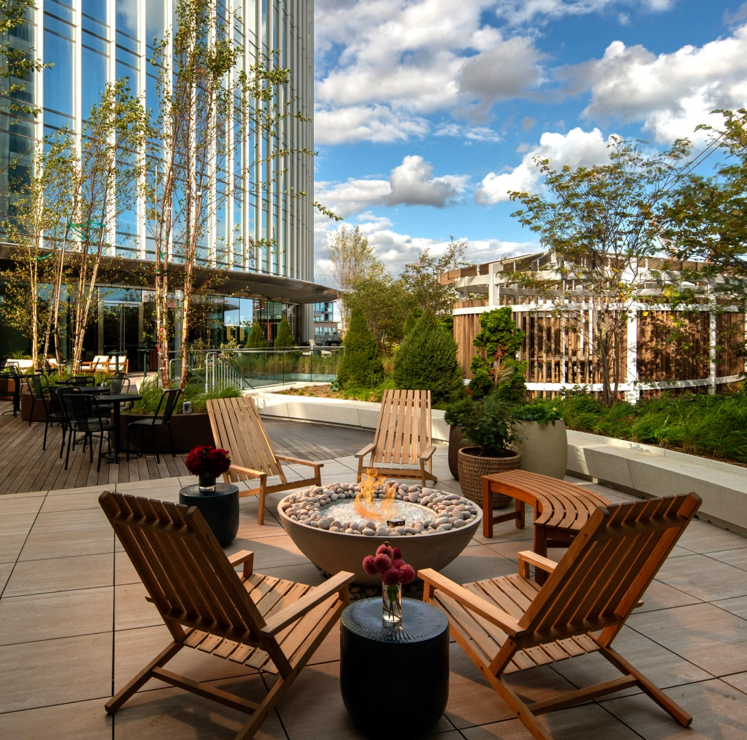 Rooftop outdoor terrace with circular fire pit wooden lounge chairs and landscaped modern office setting