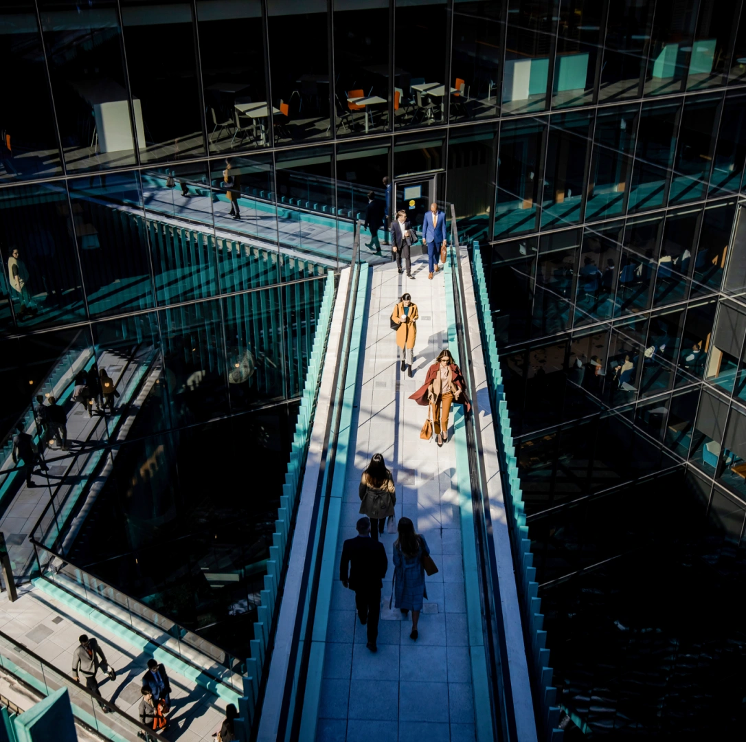 People commuting through glass walkway connecting floors in contemporary corporate office interior