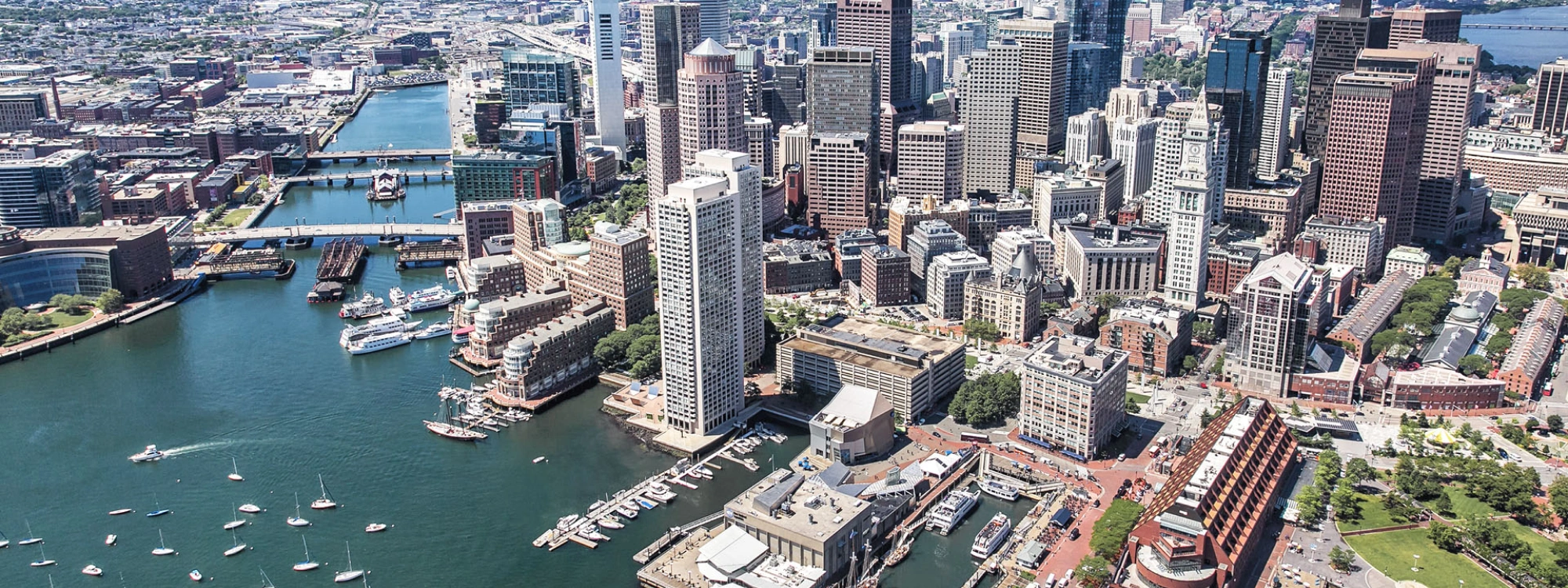 Urban coastal cityscape featuring dense skyscrapers, marina docks, and historic downtown architecture