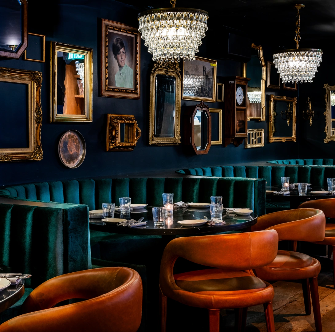 Upscale dining room featuring emerald velvet seating, leather chairs, and dramatic chandelier lighting