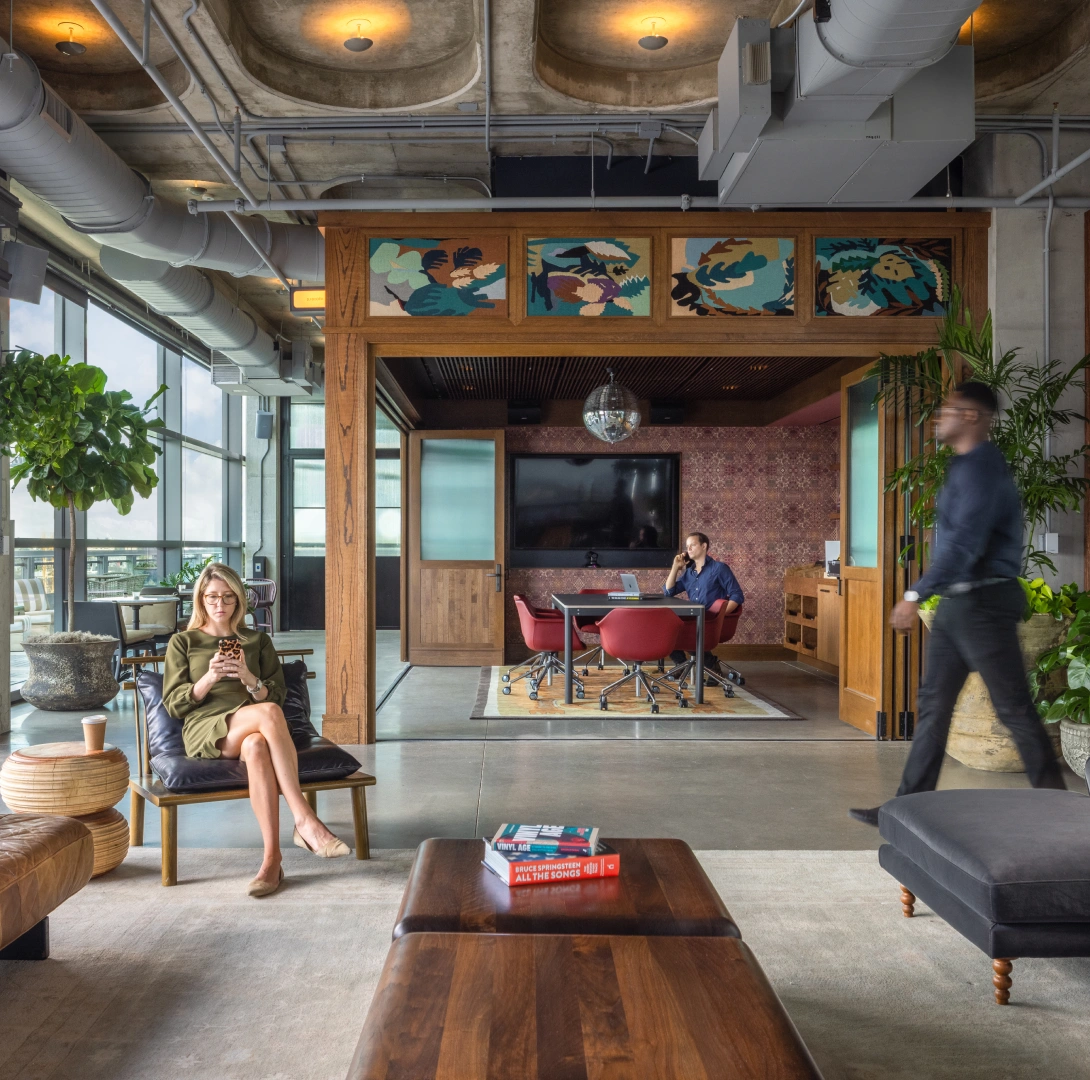 Modern coworking space featuring lounge seating enclosed meeting room plants and exposed concrete
