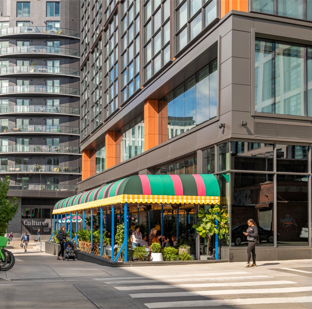 Lively urban streetscape featuring outdoor dining canopy at base of modern glass office tower