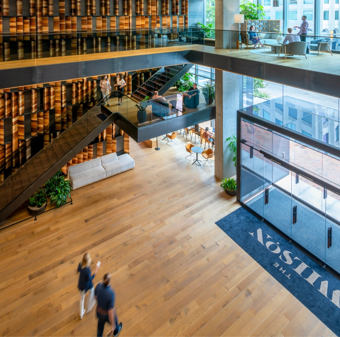 Multi level office lobby with glass staircases wood floors and collaborative seating areas