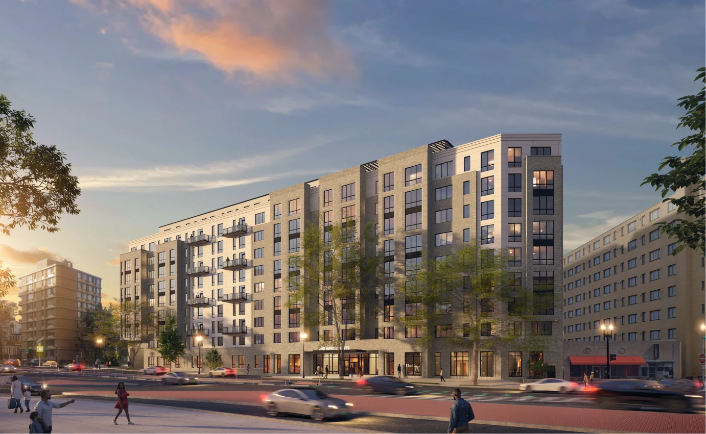 Contemporary urban residential complex featuring glass balconies, landscaped sidewalks, and cars driving past at sunset